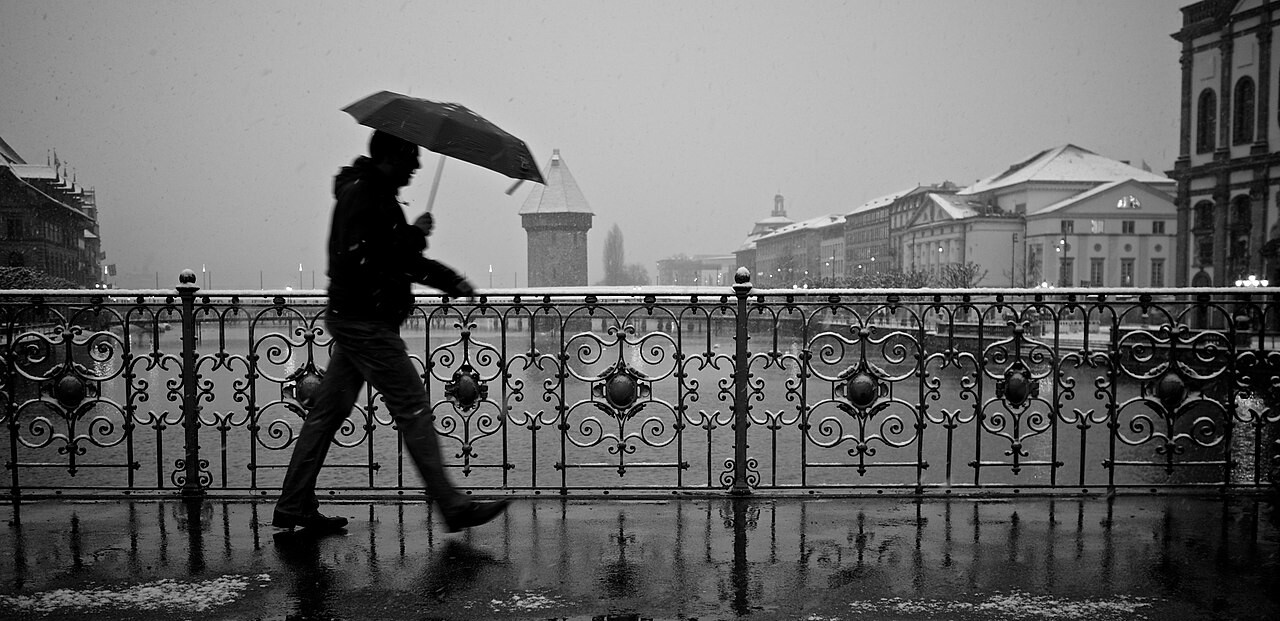 Guy_with_an_umbrella_battling_rain_and_snow_on_a_bridge.jpg